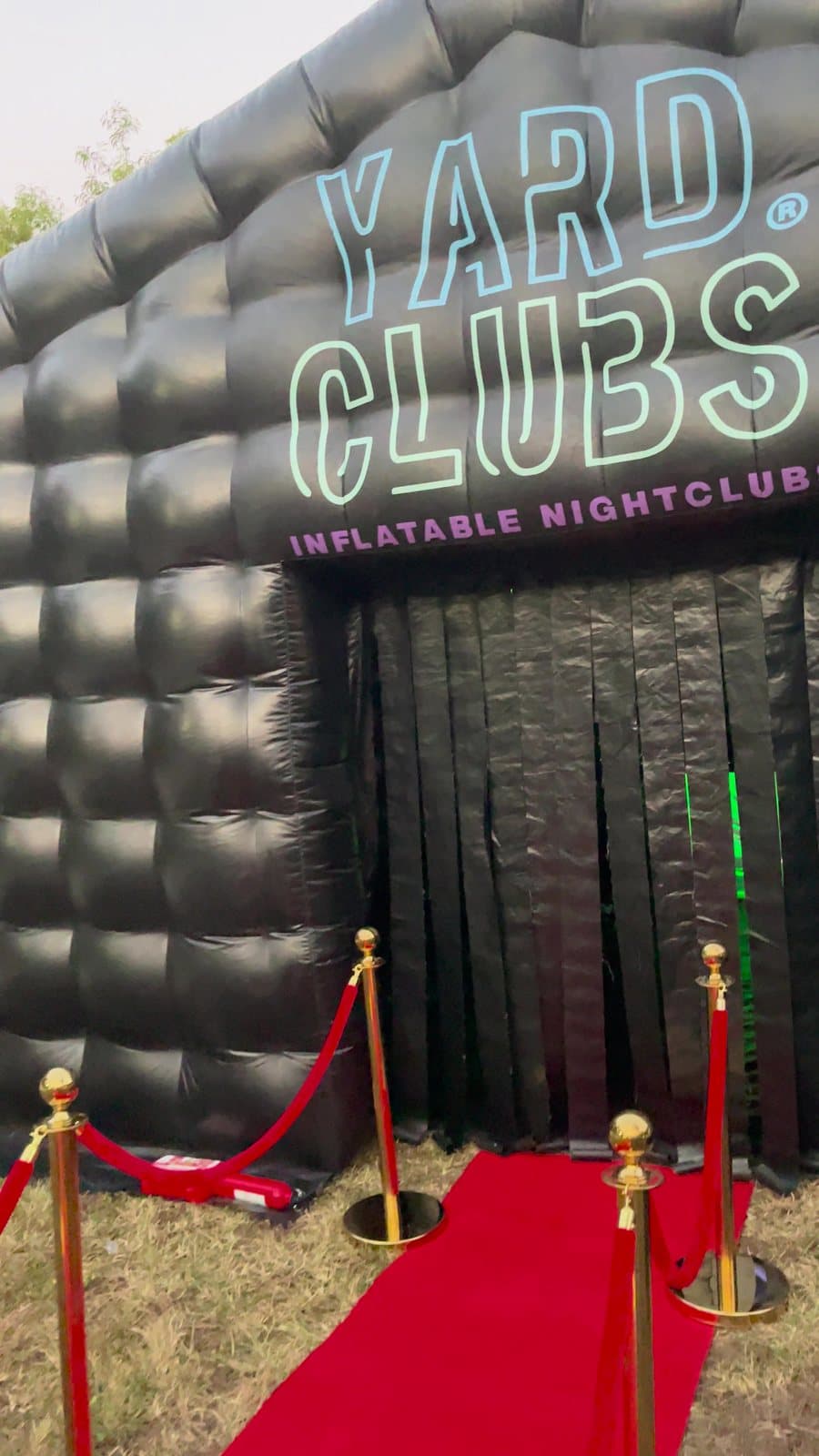 The club's sign and curtain door with brass stanchions and a red carpet in daylight