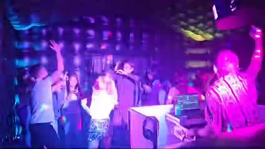 Guests with their hands up on the dance floor, the DJ booth in front