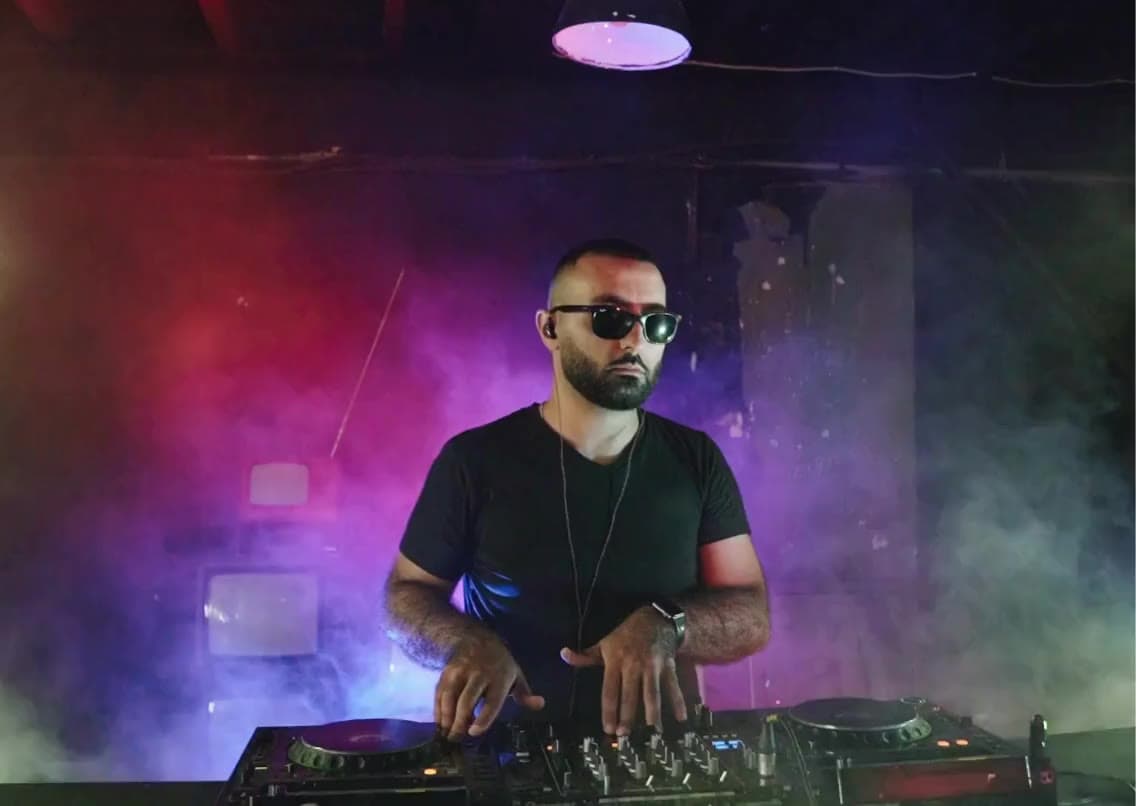 A DJ in sunglasses mixing on a controller in colored stage fog